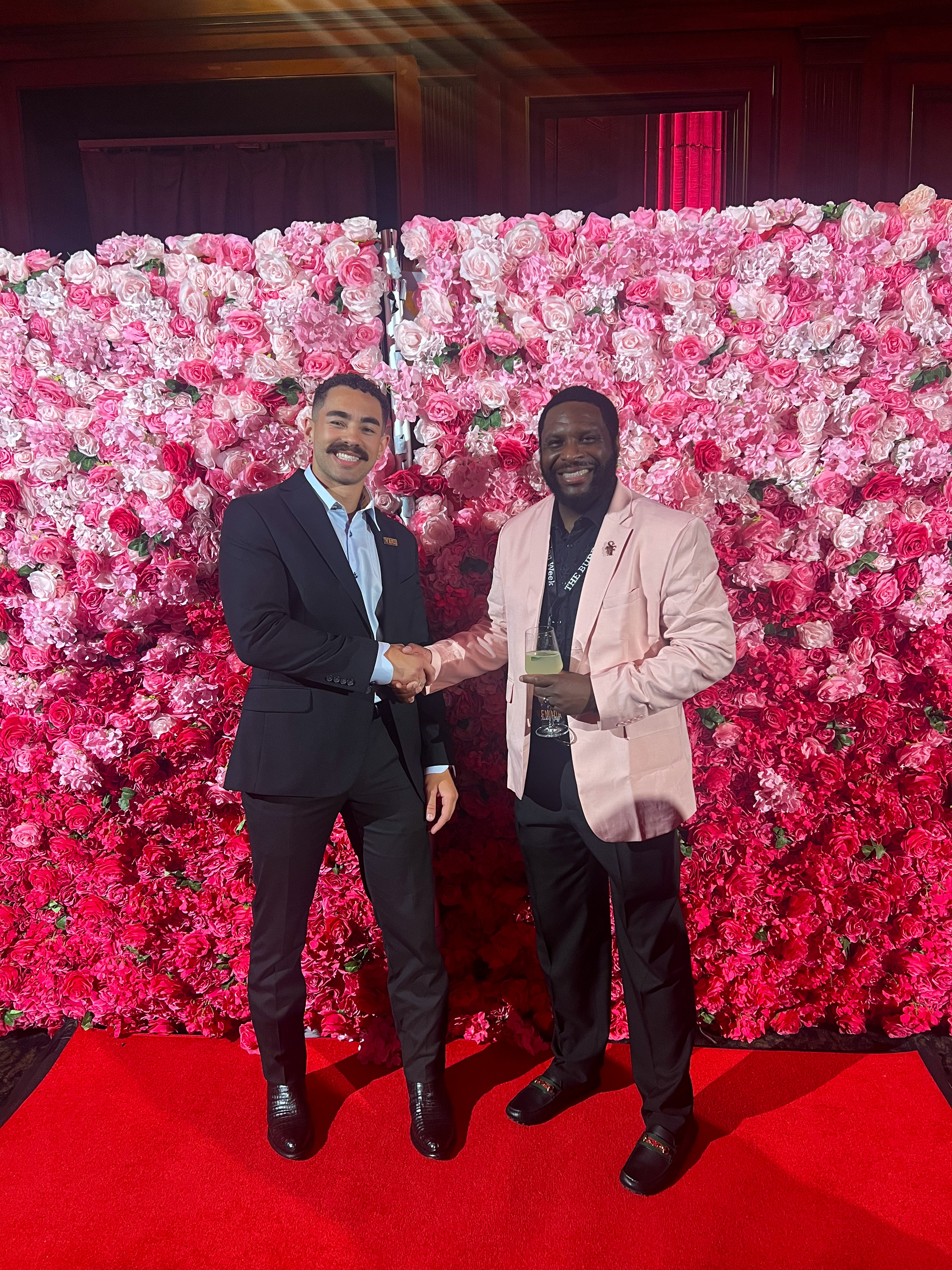 Reece Sterling greeting a colleague at a fashion industry event in front of a pink flower wall